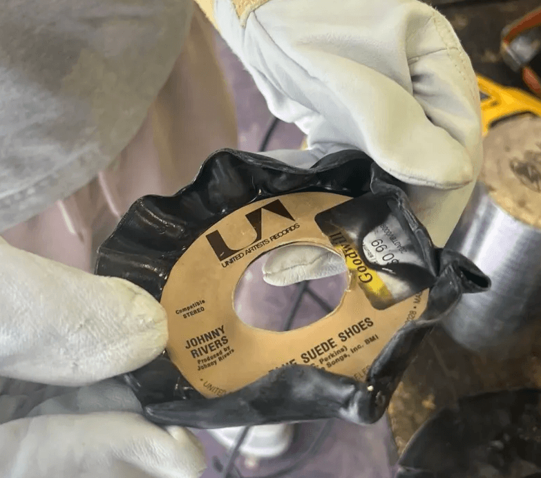 A warped 45 RPM vinyl record showing deformation from heat treatment, being too small for functional use